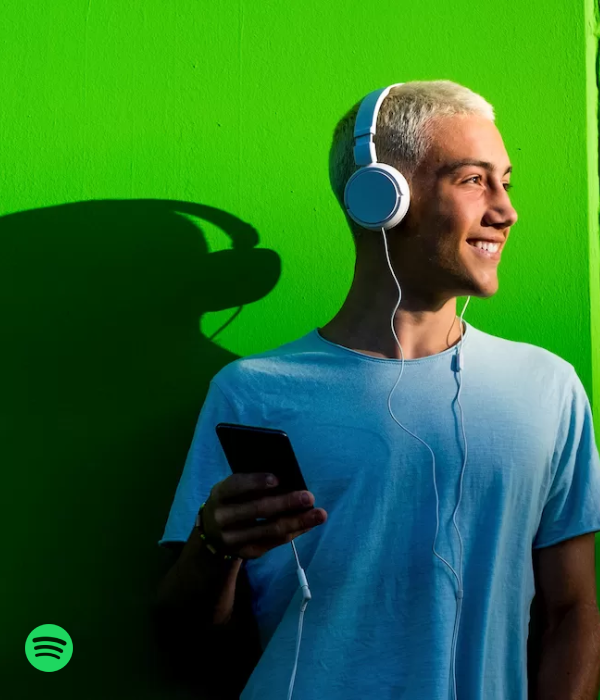Young man smiling while listening to music on headphones, representing the vibe of discovering new tracks after you buy Spotify plays.