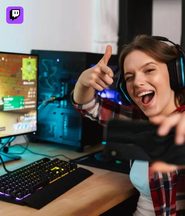 Streamer giving a thumbs up with dual monitors in the background, celebrating a viewer spike after using Twitch viewer boost services